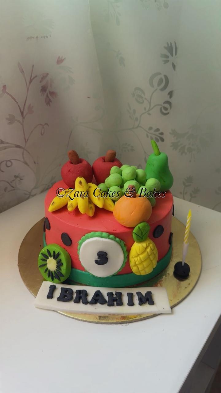 Colorful watermelon themed birthday cake with fondant fruits, number 3 topper, and custom name plaque for Ibrahim.