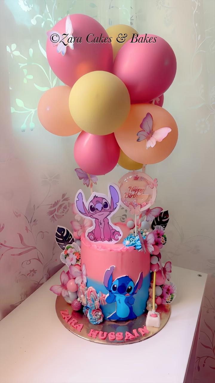 Pink and blue ombre birthday cake featuring Stitch and Angel toppers, pastel balloons, butterflies, and floral decorations