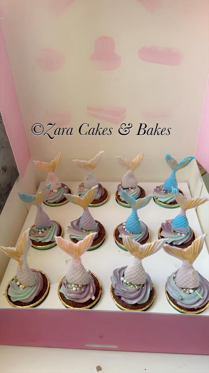 Pastel mermaid tail cupcakes with purple and blue frosting swirls and edible pearls in a pink box.