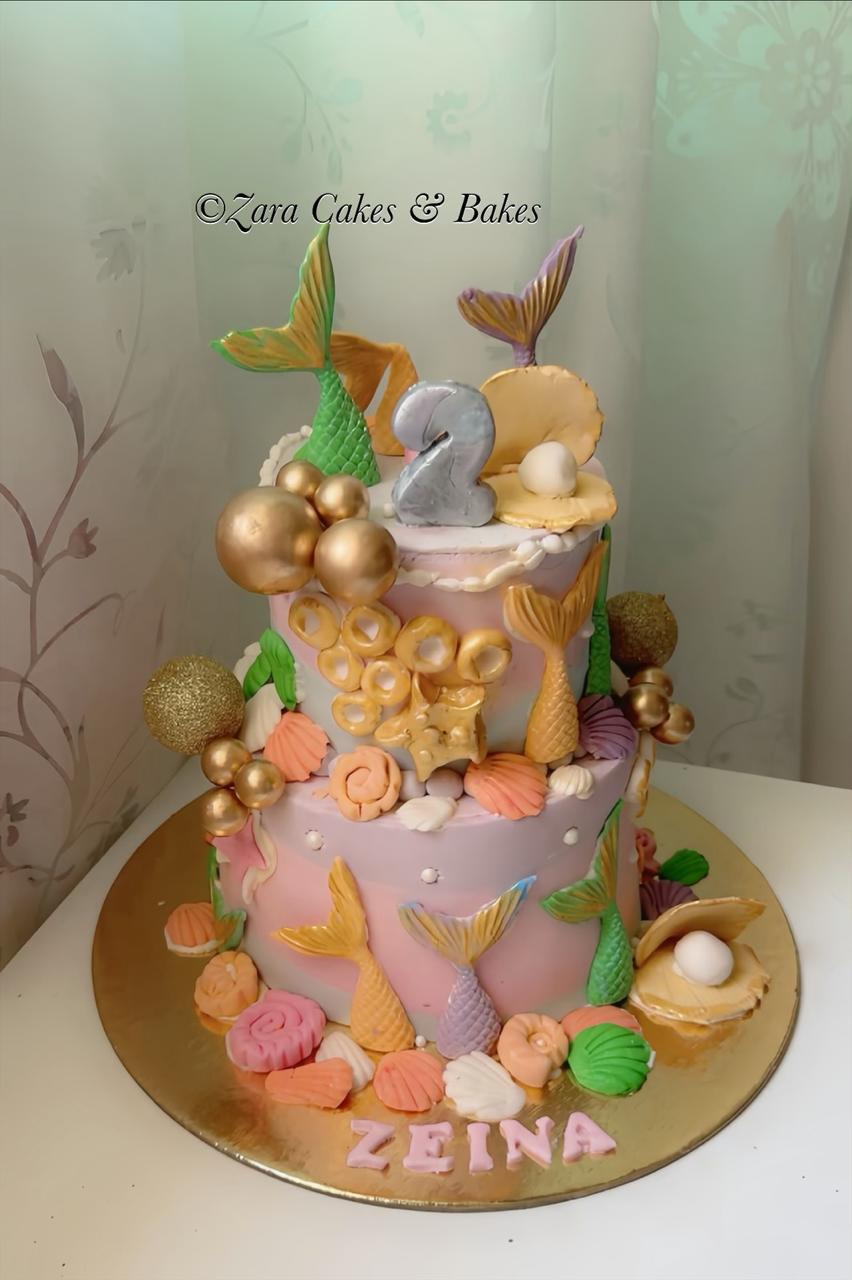 Two-tier mermaid birthday cake with fondant tails, gold seashells, and pearl decorations