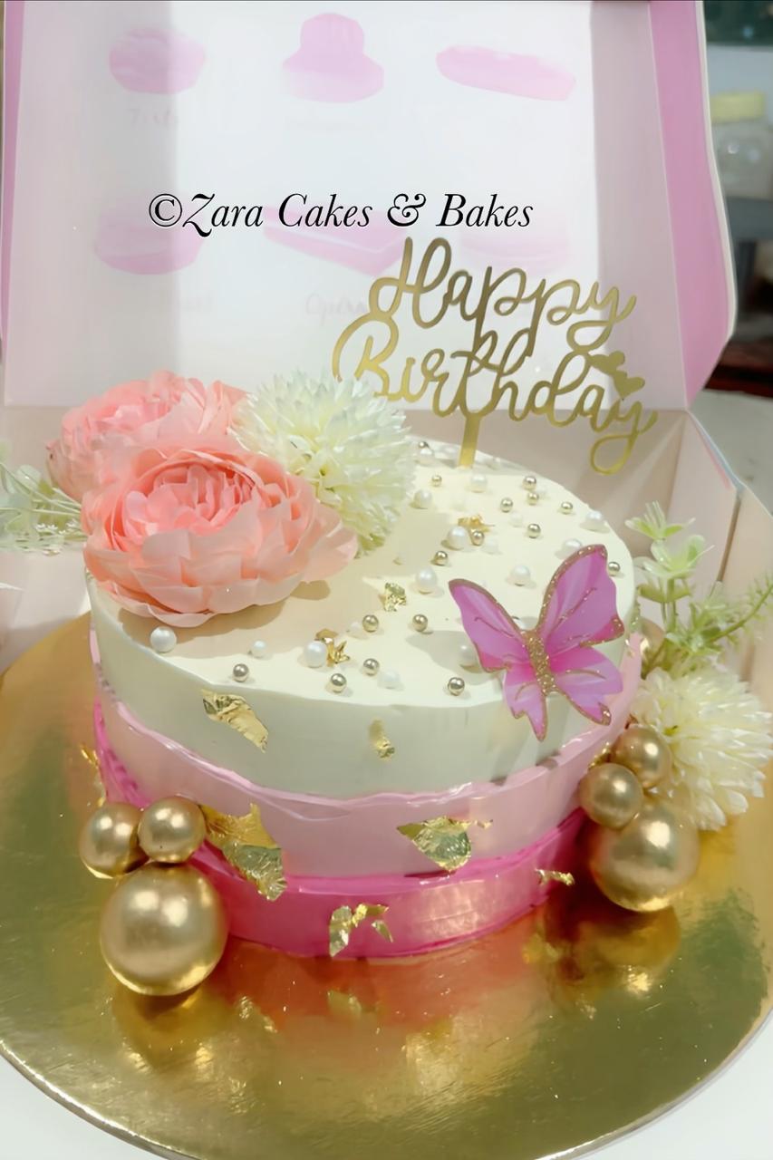 Elegant pink and white birthday cake with gold leaf, pearl decorations, and floral topper