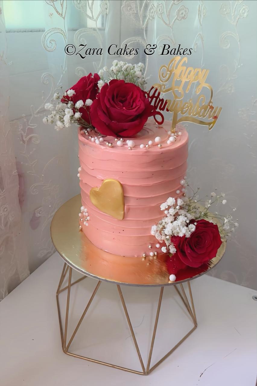 Pink textured buttercream anniversary cake with red roses, gold heart topper, and pearl decorations
