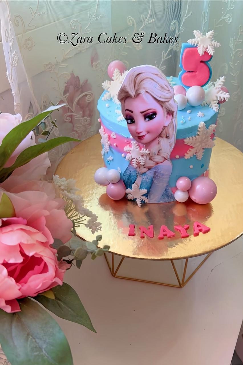 Elsa Frozen themed birthday cake with blue pink frosting snowflakes and number 5 topper for Inaya