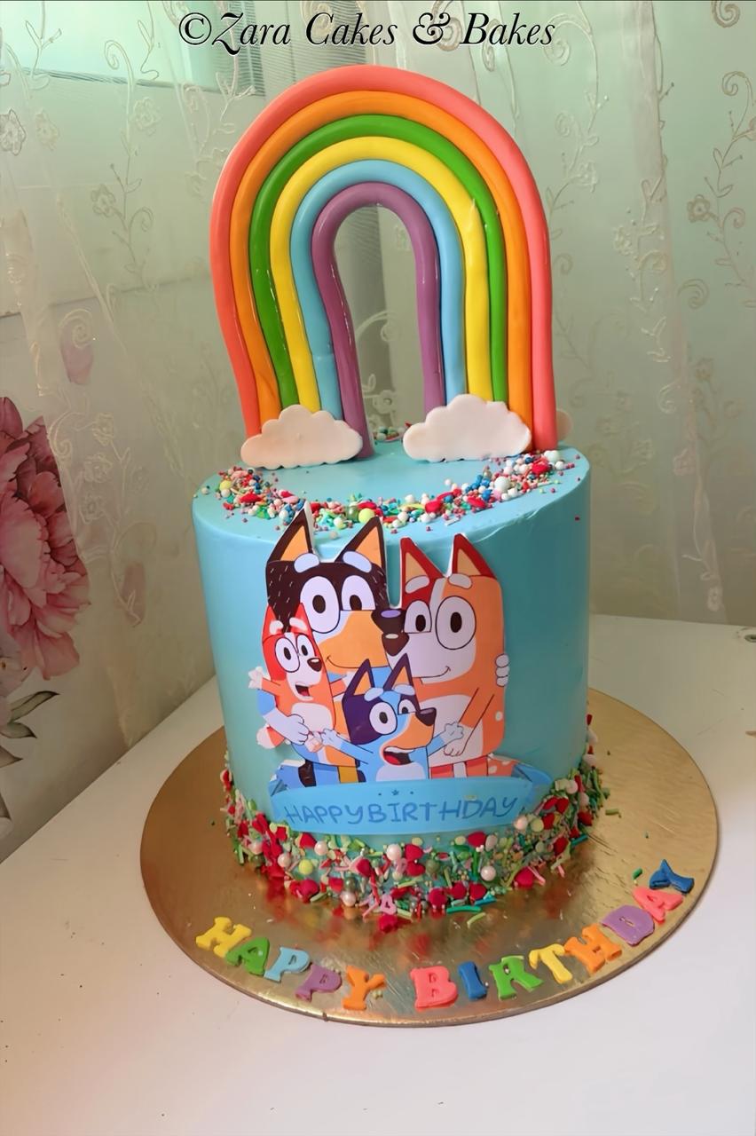Bluey themed birthday cake with blue buttercream, fondant rainbow topper, and colorful sprinkles