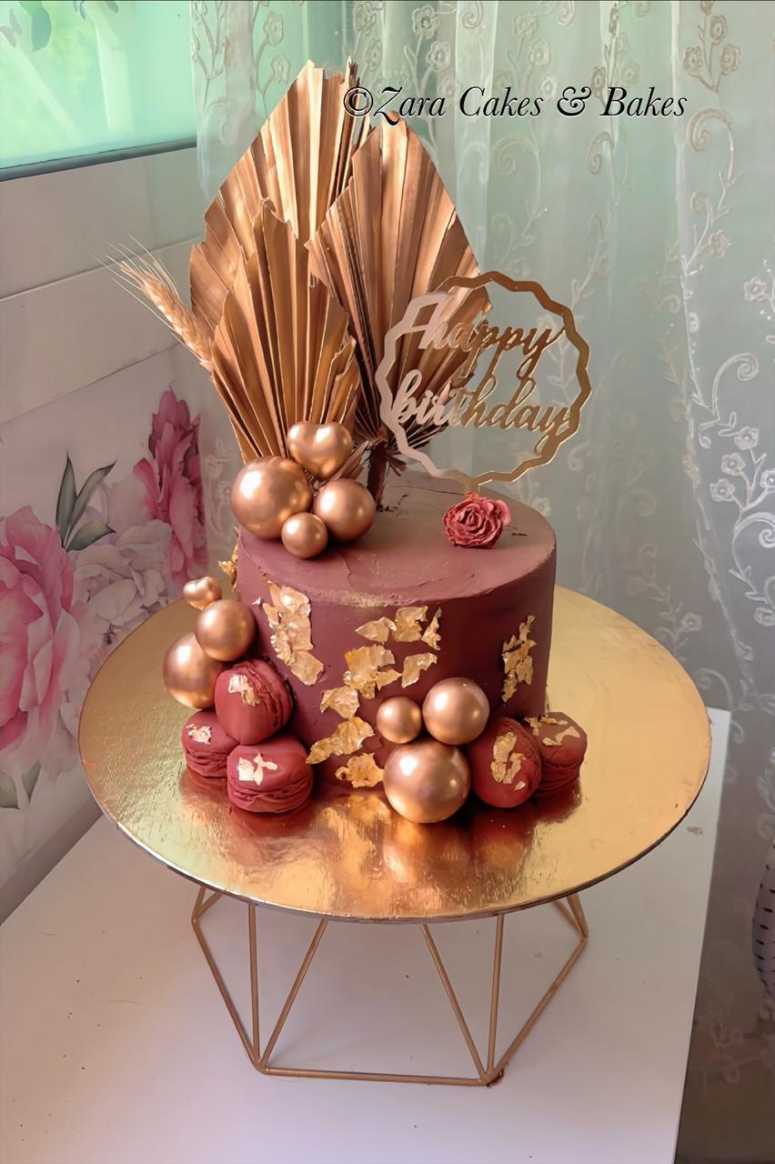 Rose gold drip birthday cake with macarons and gold leaf — signature creation by ZARA Cakes & Bakes bakery