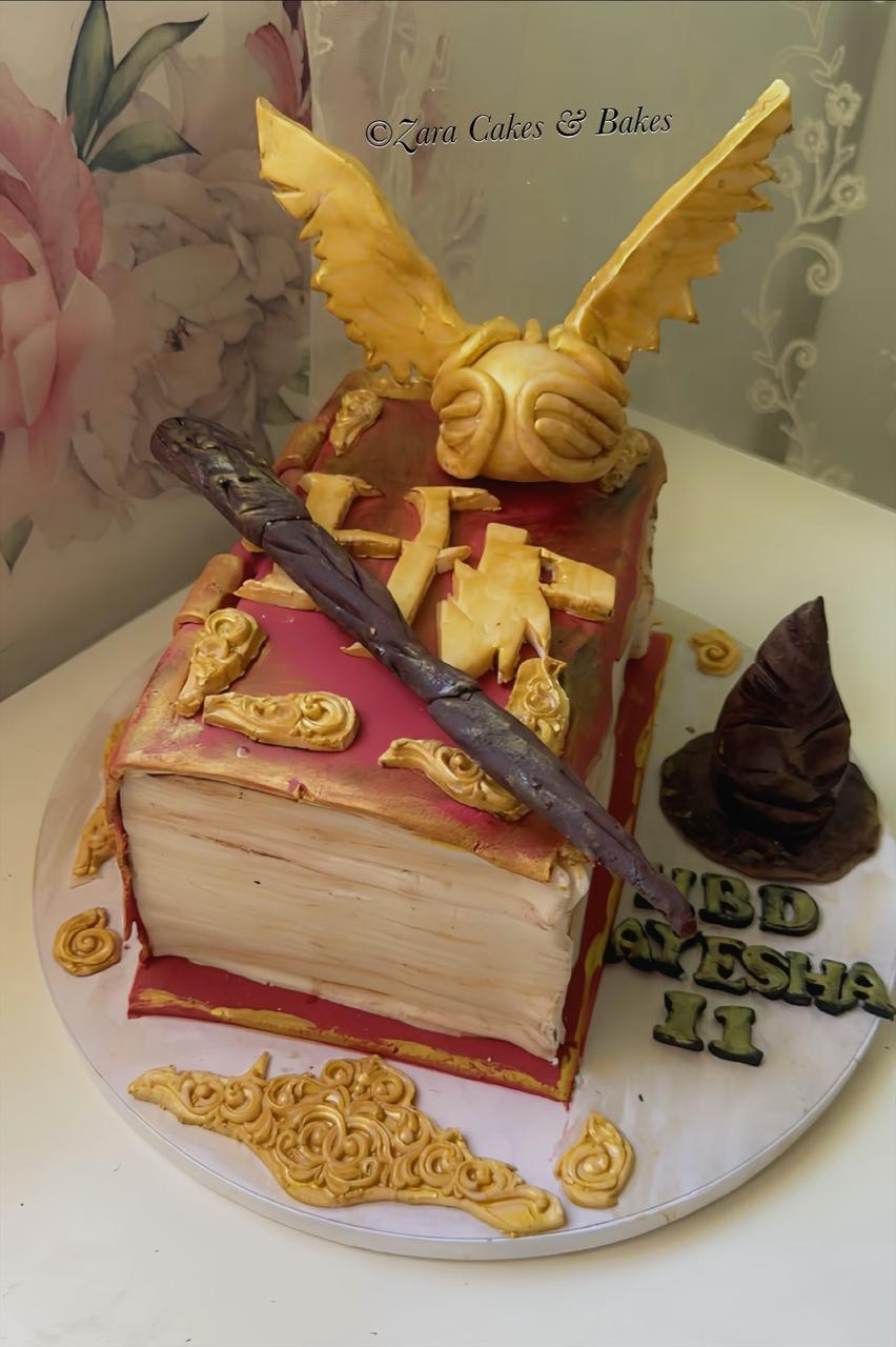 Harry Potter themed book cake with golden snitch, wand, and sorting hat decorations for birthday