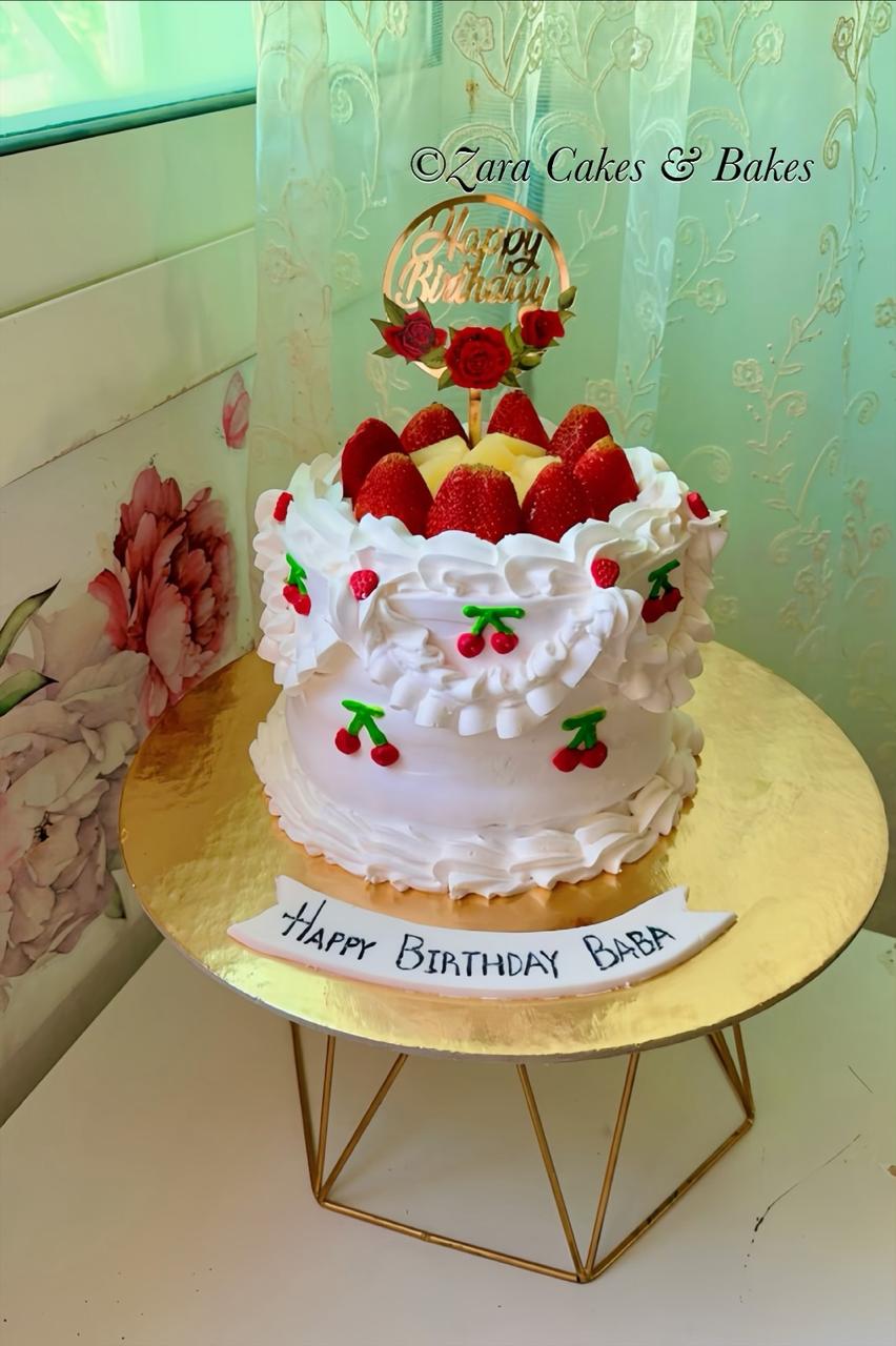 White buttercream ruffle birthday cake with fresh strawberries, cherry decorations, and gold Happy Birthday topper