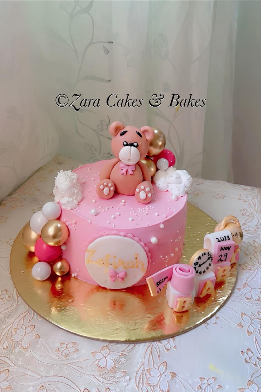 Pink fondant baby shower cake with teddy bear topper, gold balloons, and birth date blocks