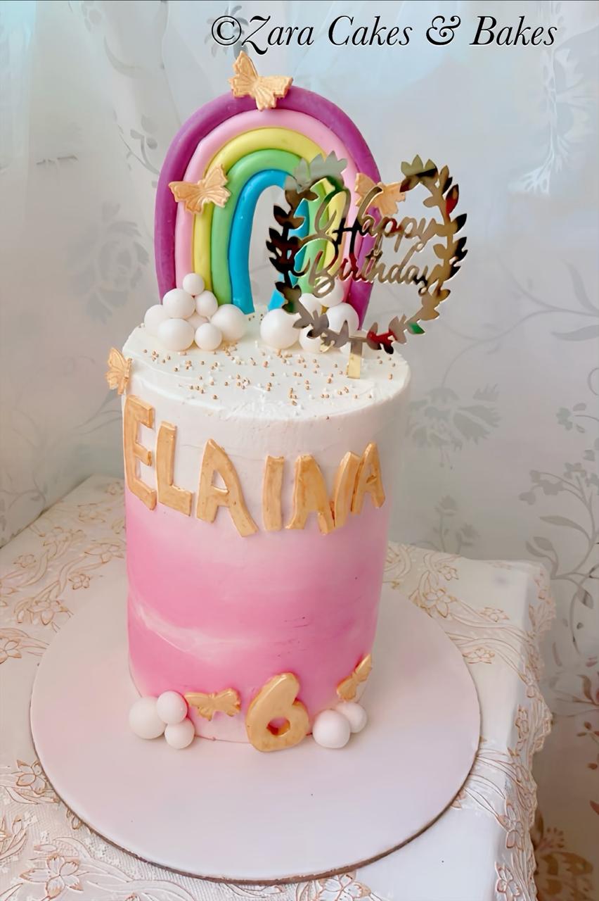 Pink ombre birthday cake with rainbow topper, gold butterflies, and custom name lettering