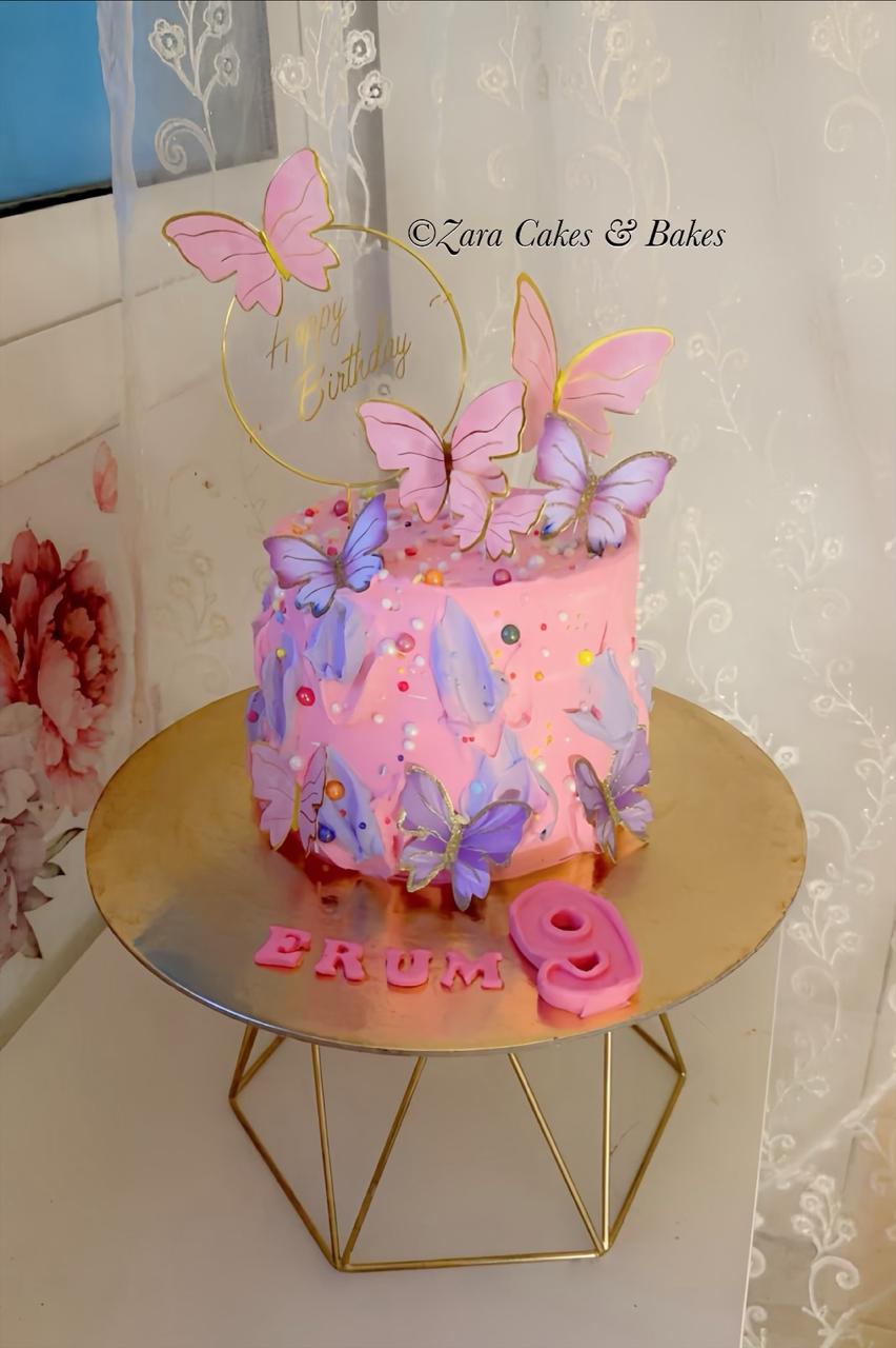 Pink buttercream birthday cake with purple butterfly toppers, gold happy birthday sign, and name Erum
