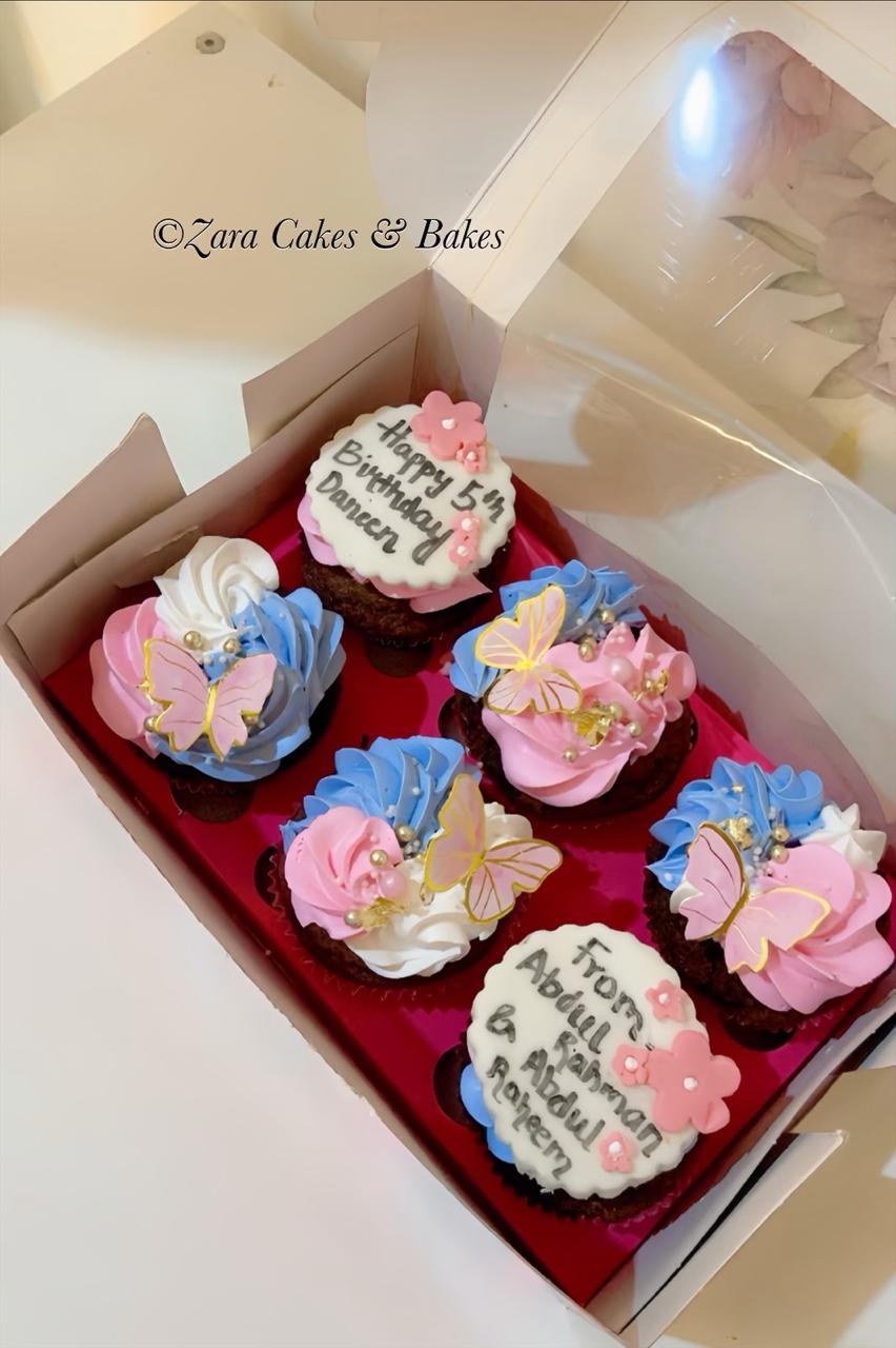 Pastel pink and blue birthday cupcakes with edible butterflies and custom toppers in a gift box