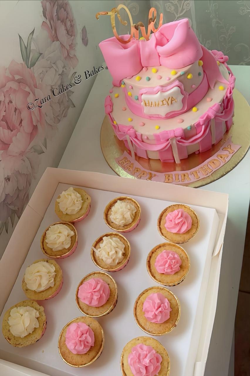 Pink fondant first birthday cake with large bow and matching vanilla cupcakes for girl's party