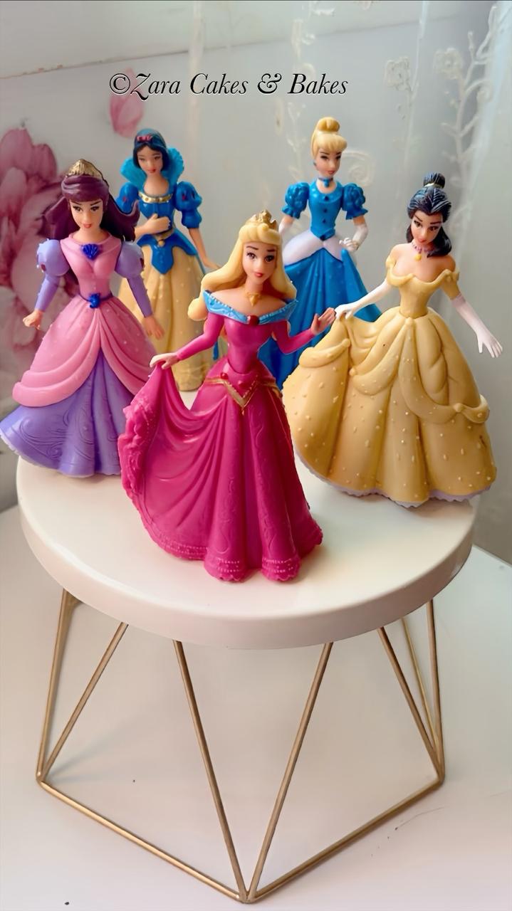 White fondant birthday cake topped with Disney princess figurines including Aurora and Belle on gold stand