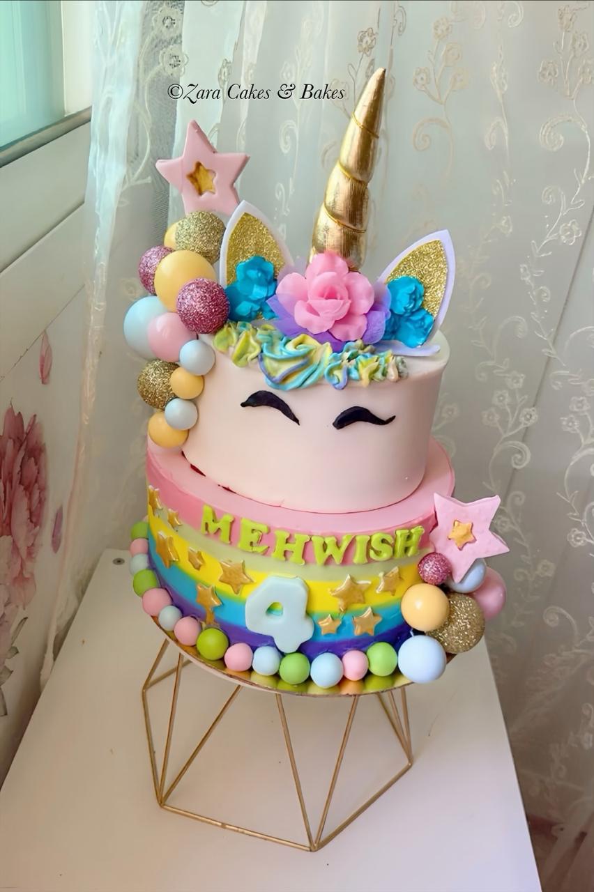 Two-tier rainbow unicorn birthday cake with gold horn, fondant ears, and colorful candy decorations for a magical celebration.