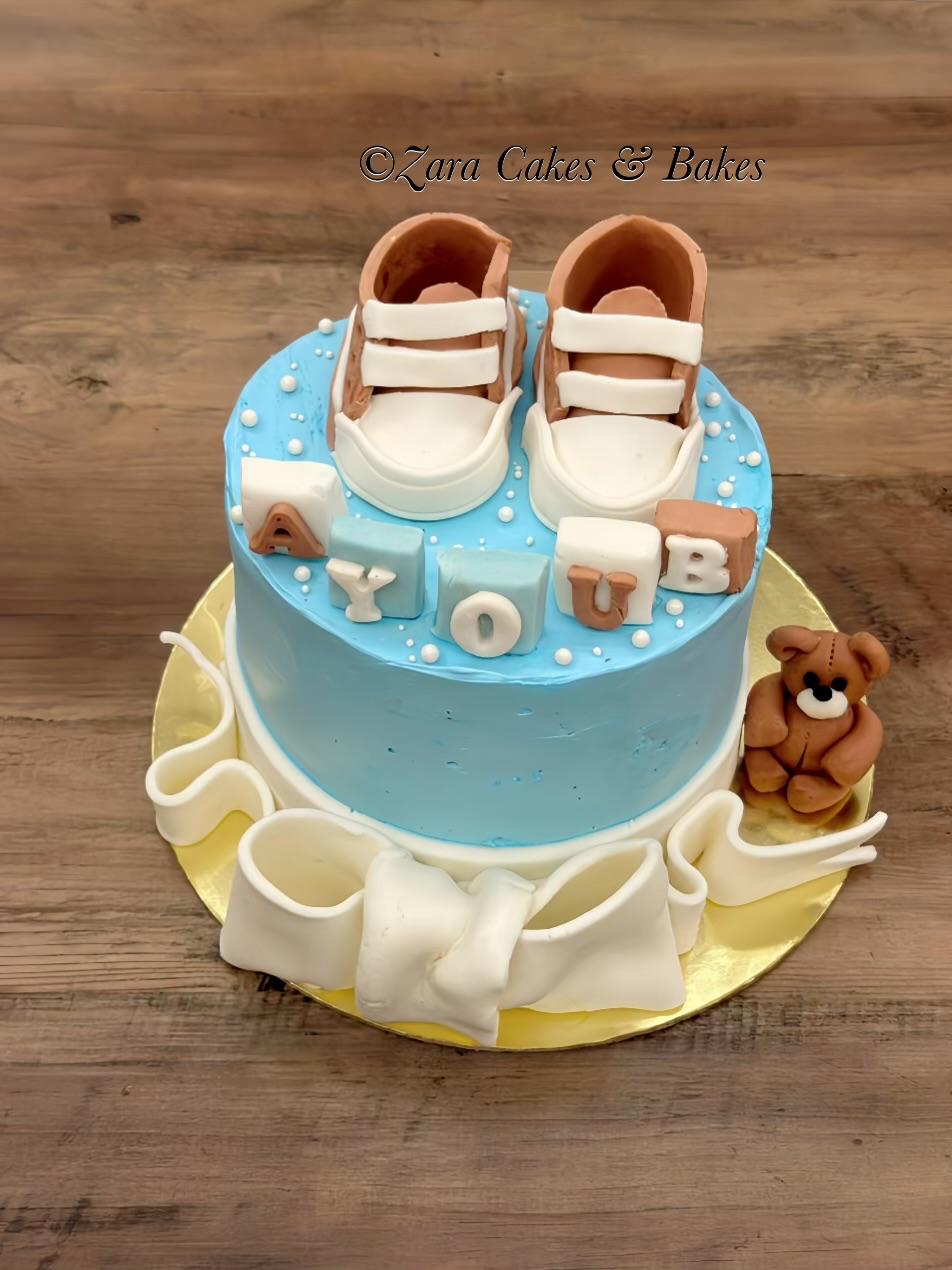 Blue buttercream baby shower cake with fondant booties, letter blocks and teddy bear decoration