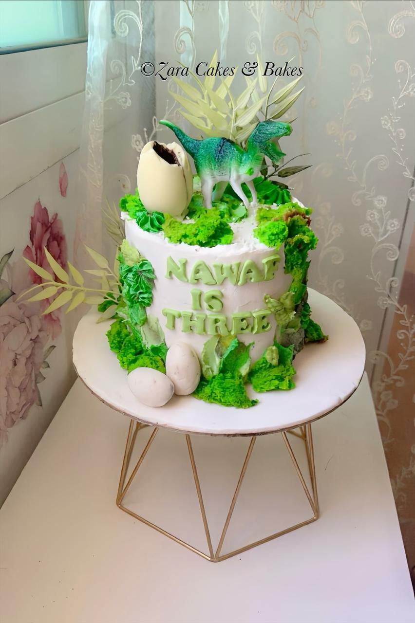 White buttercream dinosaur birthday cake with green moss, toy T-Rex and chocolate eggs