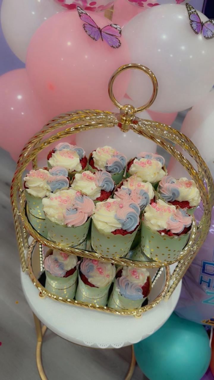 Pastel red velvet cupcakes with swirled frosting on a gold tiered stand by Zara Cakes.