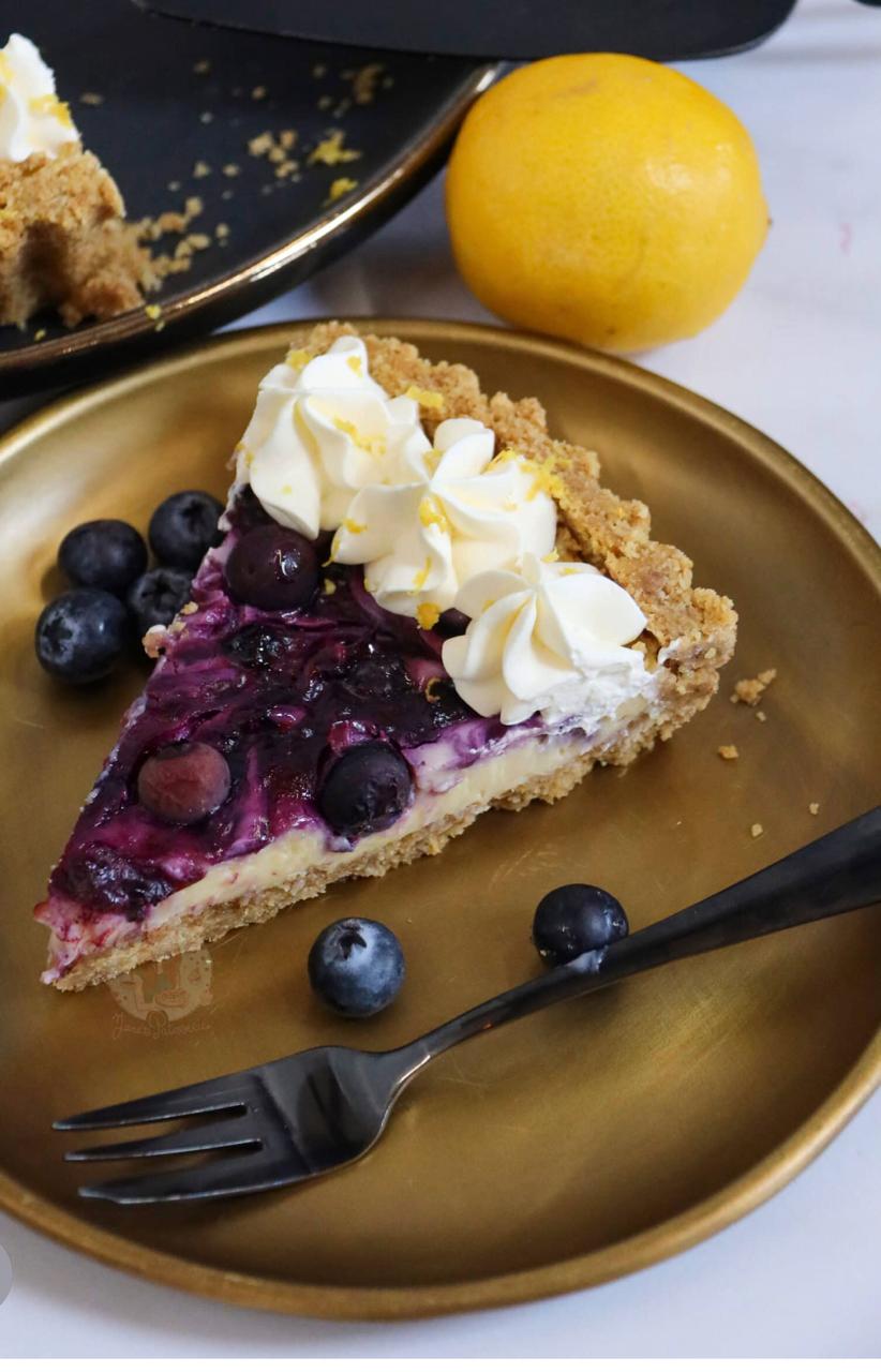 Delicious slice of lemon blueberry cheesecake tart with fresh cream on a gold plate.